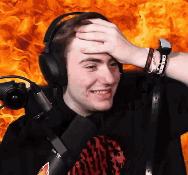 a man wearing headphones and a watch holds his hand to his forehead in front of a fire background