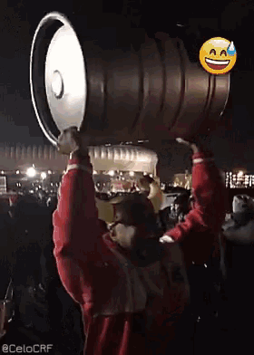 a man in a red jacket is holding a large keg over his head with a smiley face on it