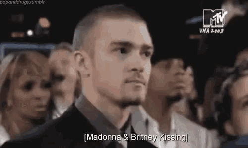 a man in a suit and tie is standing in front of a crowd of people and talking about madonna and britney spears .