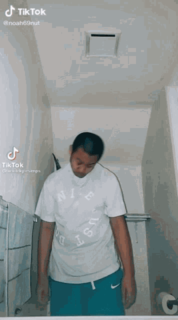 a man wearing a white nike shirt is standing in a bathroom