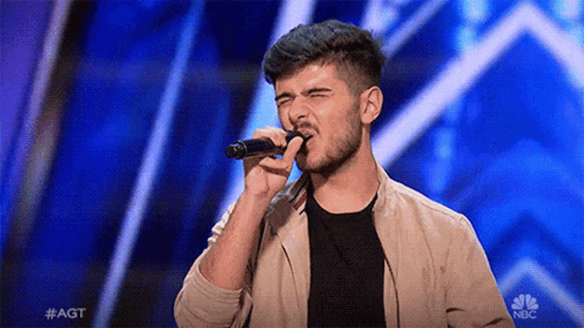 a young man is singing into a microphone on nbc 's agt show