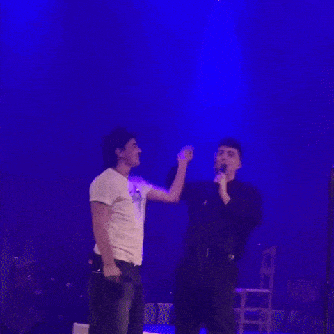 a man singing into a microphone while another man holds his arm up