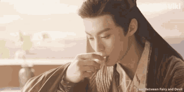 a man with long hair is drinking from a glass with the words love between fairy and devil written above him