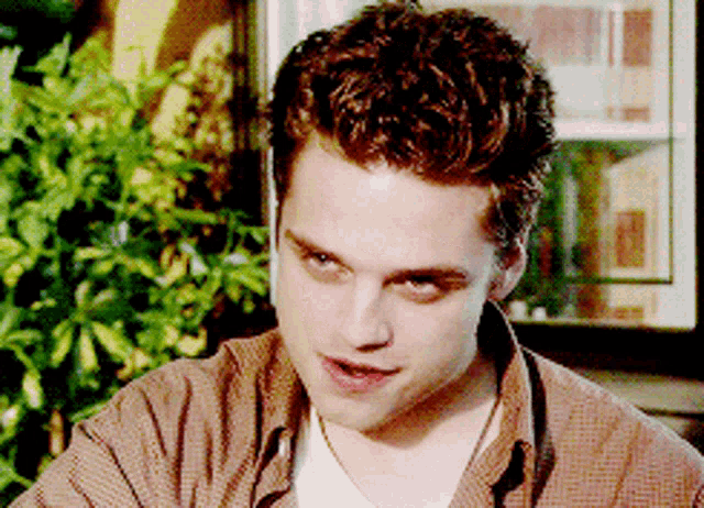a young man with curly hair is wearing a brown shirt and white shirt