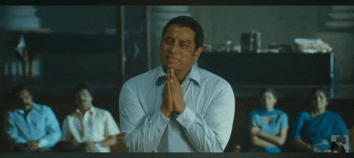 a man in a white shirt is praying with his hands folded in front of a group of people