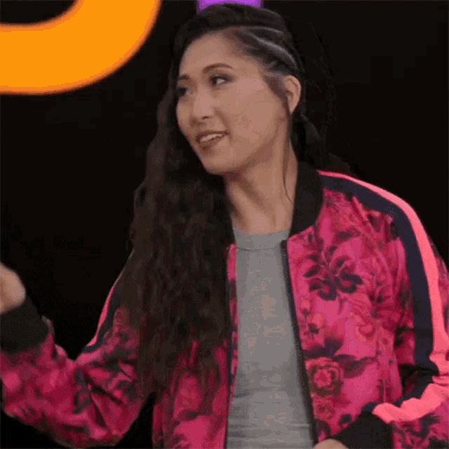 a woman wearing a pink bomber jacket with a floral pattern is dancing .