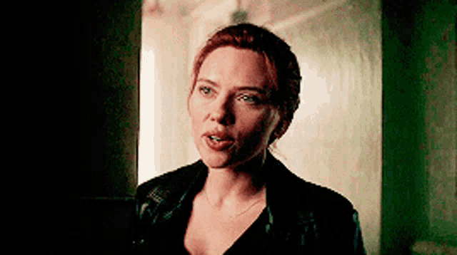 a woman with red hair is wearing a black jacket and standing in a dark room .