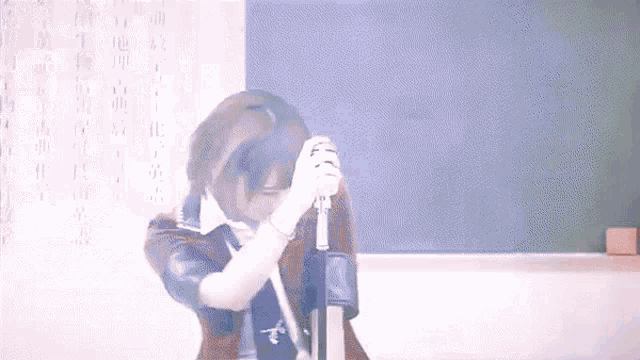 a woman is singing into a microphone in front of a blackboard