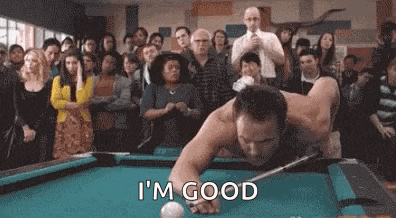 a man without a shirt is playing pool in front of a crowd of people .
