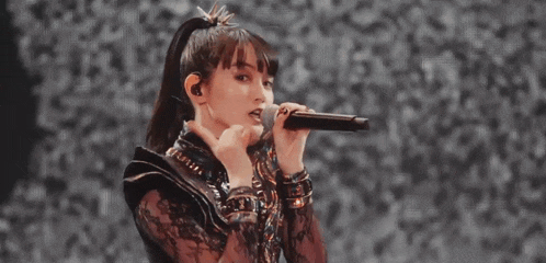a woman is singing into a microphone and making a heart with her hands .
