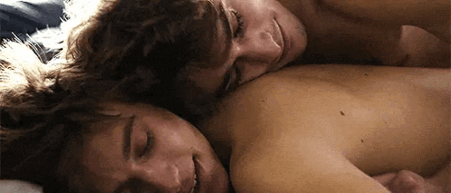 two men are laying next to each other on a bed and hugging each other .