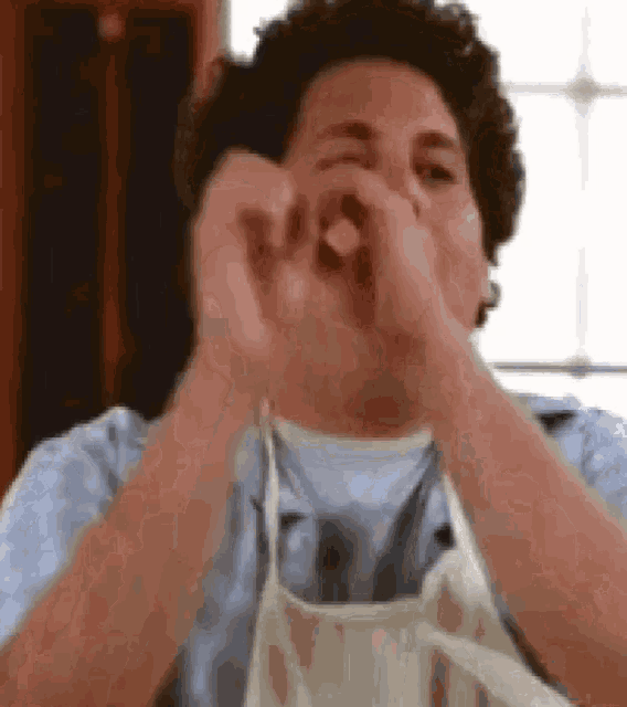 a man wearing an apron is covering his mouth with his hands .