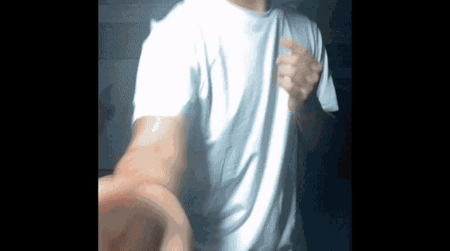 a man wearing a white t-shirt is standing in the dark