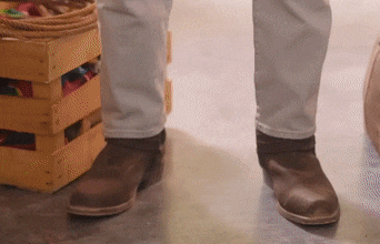 a person wearing brown boots standing in front of a wooden box