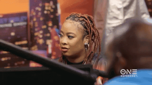 a woman with red braids is sitting in front of a screen that says one