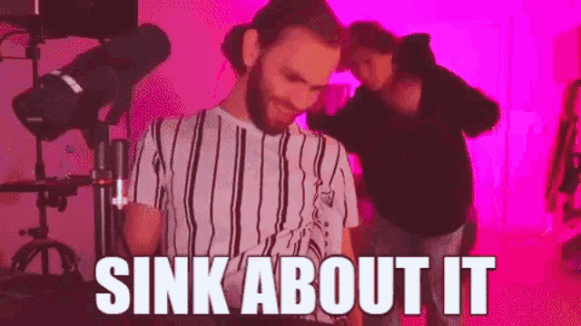 a man with a beard is standing in front of a microphone with the words `` sink about it '' written on the screen .
