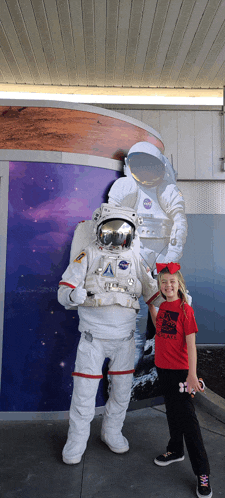 a girl in a red shirt stands next to an astronaut in a nasa outfit