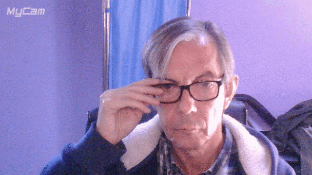 a man adjusts his glasses in front of a mycam sign