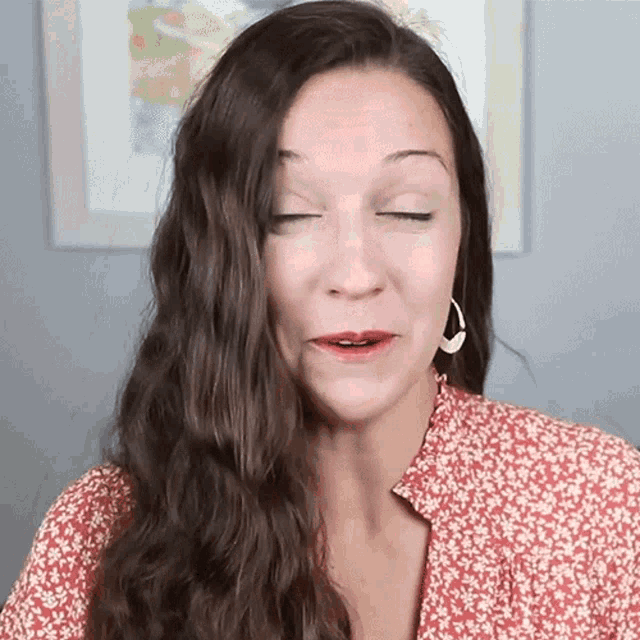 a woman with her eyes closed is wearing a red floral shirt and earrings