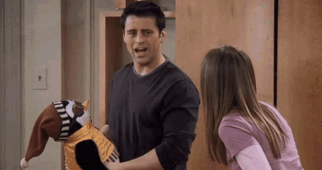 a man in a black shirt is holding a stuffed animal while a woman looks on