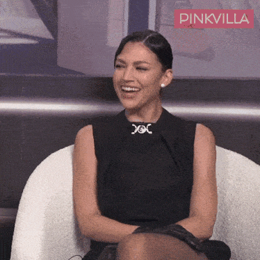 a woman in a black dress is smiling in front of a pinkvilla banner
