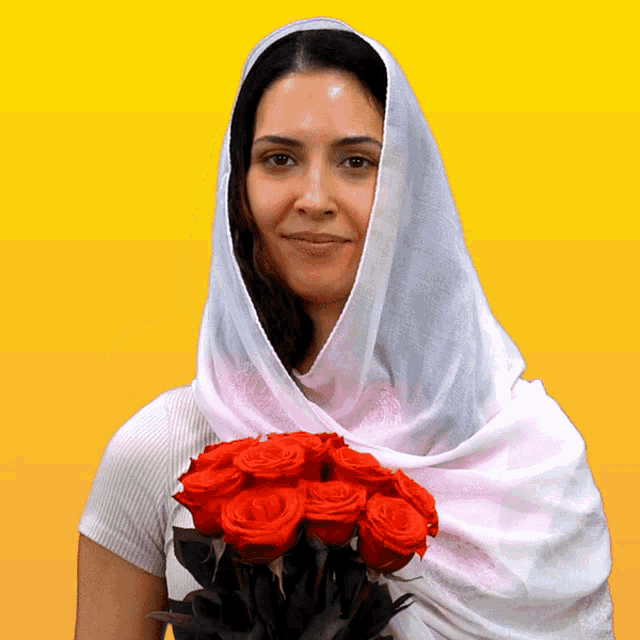 a woman wearing a white scarf holds a bunch of red roses