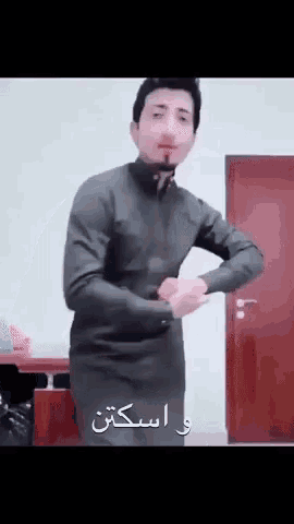 a man in a black jacket is standing in front of a door and making a funny face .