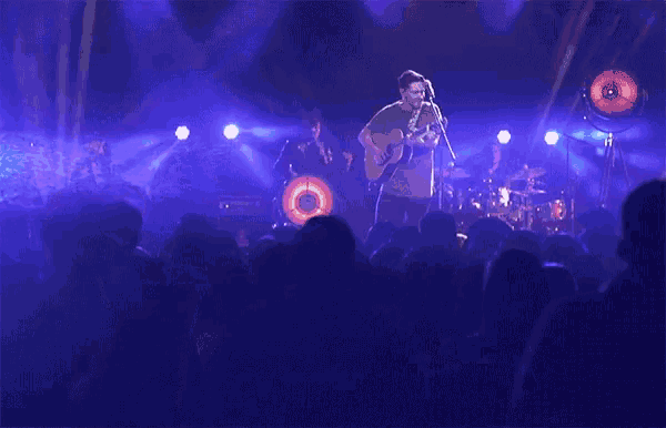 a man sings into a microphone while playing a guitar on stage