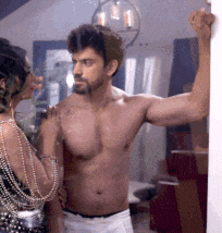 a shirtless man standing next to a woman in a room