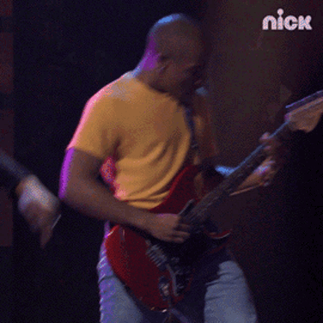 a man in a yellow shirt is playing a red guitar in front of a nick sign