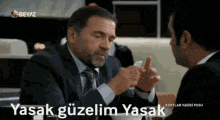 a man in a suit and tie is sitting at a table with another man .