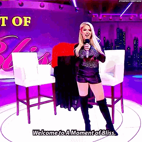 a woman stands on a stage holding a microphone and saying welcome to a moment of bliss