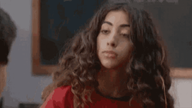 a woman with curly hair is making a face in front of a blackboard .