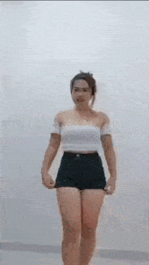 a woman is standing in front of a white wall wearing shorts and a white top .