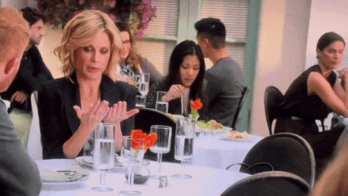 a woman sits at a table with wine glasses and flowers on it