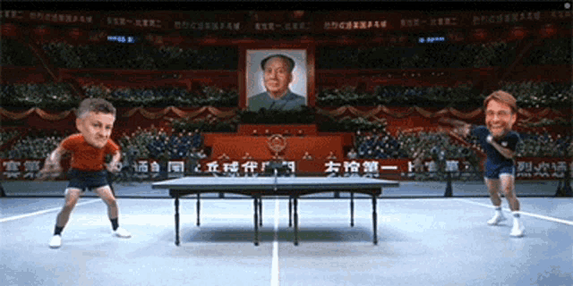 two men are playing ping pong in front of a crowd and a painting of mao zedong