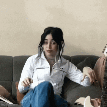 a woman in a white jacket is sitting on a couch with her legs crossed .
