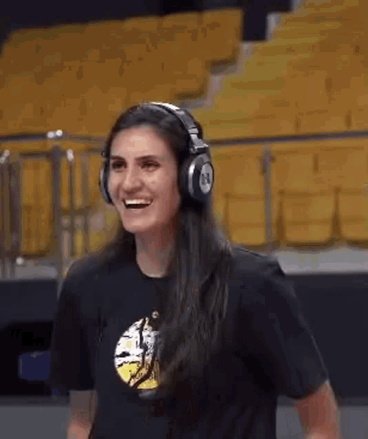 a woman wearing headphones and a black shirt is smiling in front of yellow seats .