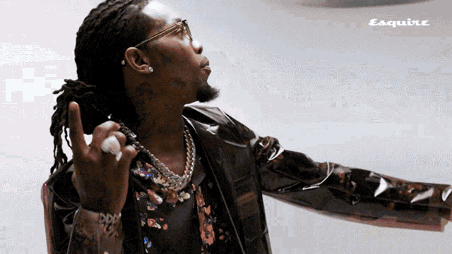 a man with dreadlocks is wearing a leather jacket and a floral shirt with esquire written on the bottom