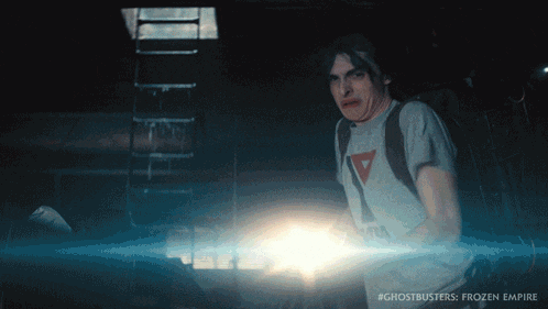 a man in a ghostbusters frozen empire shirt holds a light
