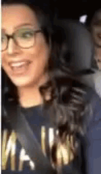 a woman wearing glasses and a blue shirt is smiling while sitting in a car .