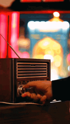 a person adjusts the volume on a radio with a neon sign in the background