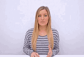 a woman in a striped shirt is sitting at a table with her eyes closed and her hands outstretched .