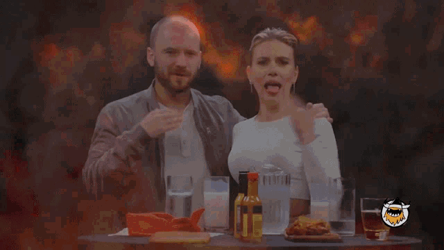 a man and a woman are sitting at a table with a bottle of hot sauce