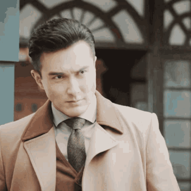 a man wearing a tan coat and tie looks to his left
