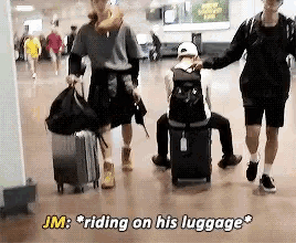 jm is riding on his luggage while a man sits on a suitcase