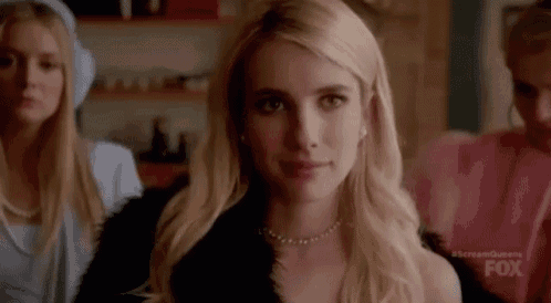 a blonde woman wearing a black fur coat and a necklace is standing in a room with two other women .