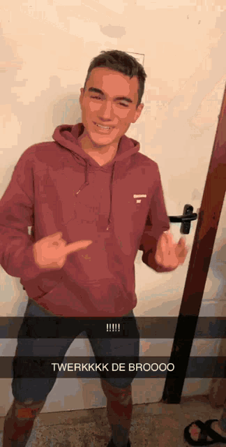 a man in a maroon hoodie is standing in front of a door and giving the middle finger