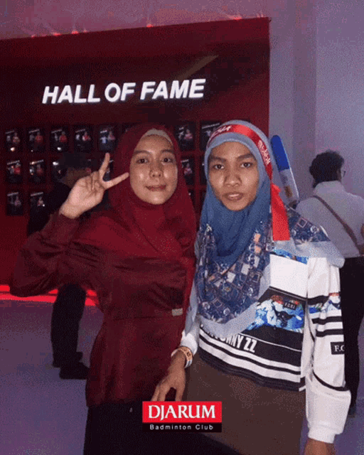 two women pose for a photo in front of a wall that says hall of fame