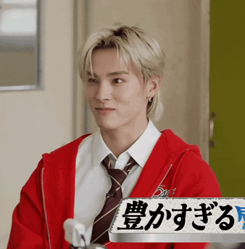 a young man wearing a red jacket and tie looks at the camera with a sign in front of him that has chinese writing on it